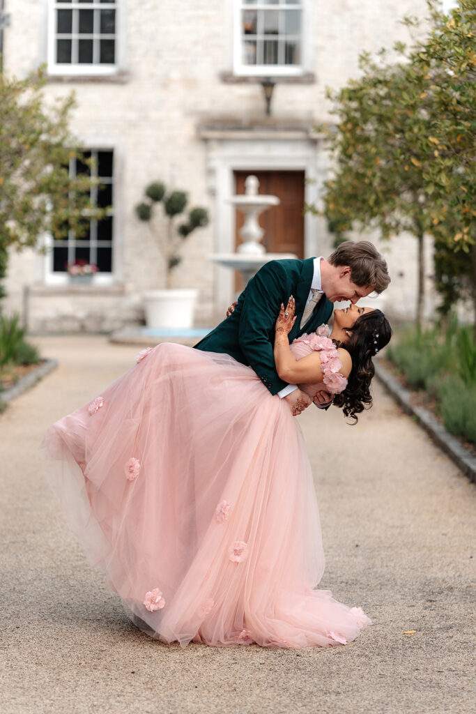 A bride and groom stop for a Hollywood kiss in front the the Manor House at Froyle Park