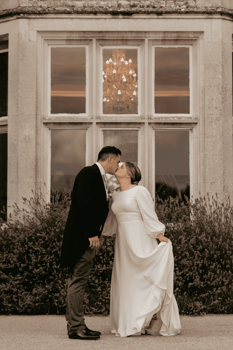 A Bride and groom share a kiss beside the lavender at Froyle Park
