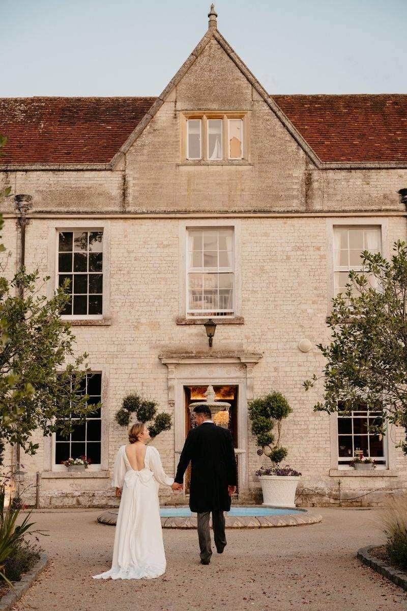 A bride and groom stroll towards the manor house at Froyle Park